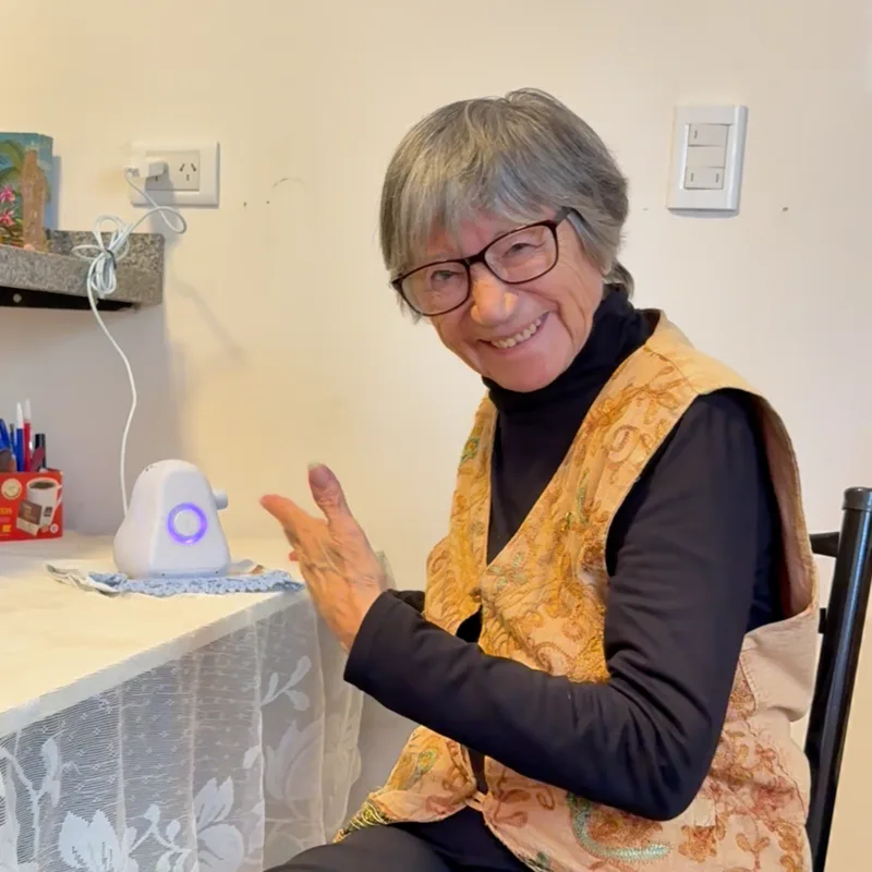 Eva, 78, smiling while seated at home